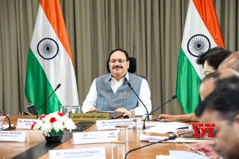 Jagat Prakash Nadda seated at the head of a conference table between two national flags, with officials and nameplates in the foreground