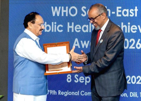 Jagat Prakash Nadda holding a framed certificate and shaking hands with Dr Tedros Adhanom Ghebreyesus in front of a WHO South-East Asia banner
