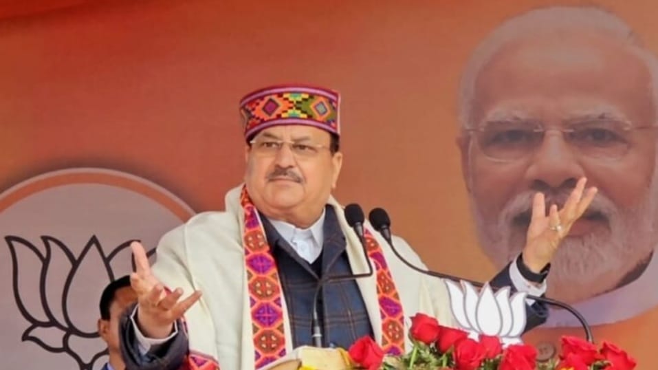 Jagat Prakash Nadda speaking at a lectern wearing a Himachali cap and shawl