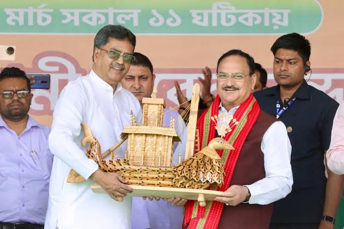 Jagat Prakash Nadda holding a bamboo-craft boat model with another dignitary on stage