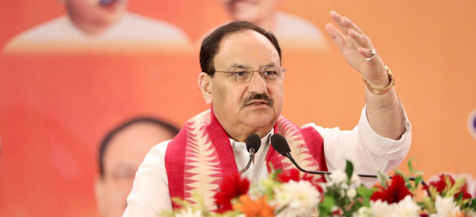 Jagat Prakash Nadda speaking into microphones with his right hand raised